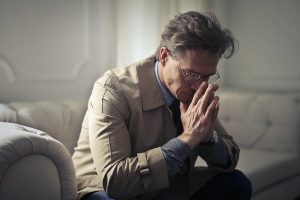 man sat on sofa with hands on mouth-min